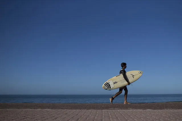 In this  May 21, 2015 photo, Gabriel Santos walks with his board after surfing at Sao Conrado beach in Rio de Janeiro, Brazil. Not long ago, many of these kids were begging on the streets or engaged in crime, but two surf schools serving youth from Rio's largest slum, Rocinha, have helped change that. (Photo by Felipe Dana/AP Photo)