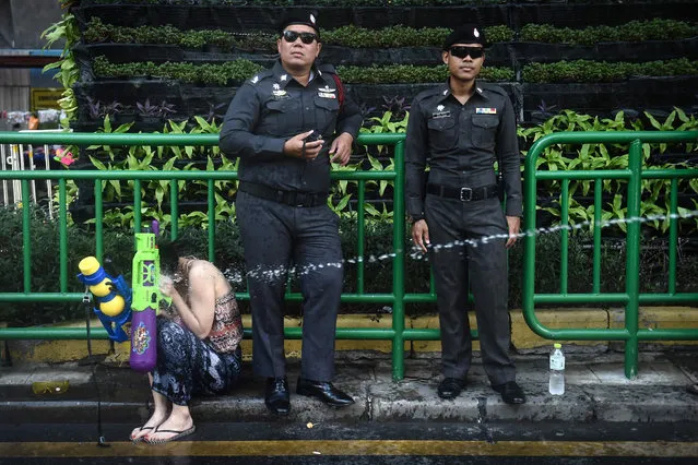 Thai policemen stand and watch as a woman is sprayed with water during Songkran, Thailand's traditional New Year festival, on Silom road in Bangkok on April 13, 2017. (Photo by Lillian Suwanrumpha/AFP Photo)