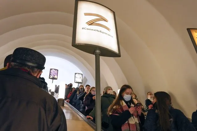 People go down the escalator past the letter Z, which has become a symbol of the Russian military, and a hashtag reading “We don't abandon our own” in an underground station in St. Petersburg, Russia, Wednesday, March 9, 2022. (Photo by AP Photo/Stringer)