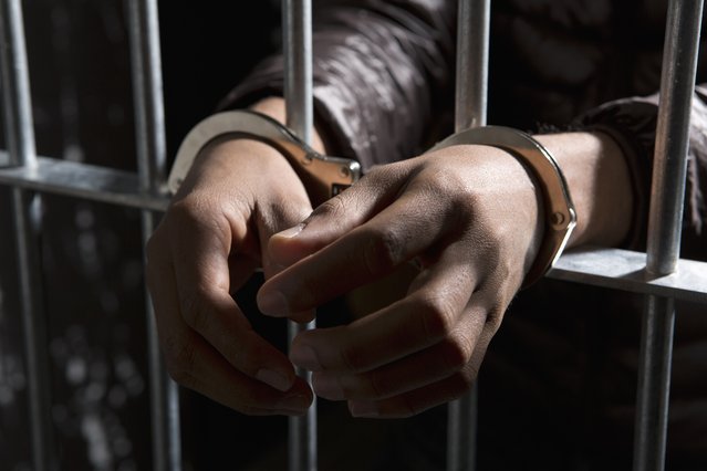 A prisoner behind bars with hands cuffed. (Photo by Caspar Benson/Getty Images)