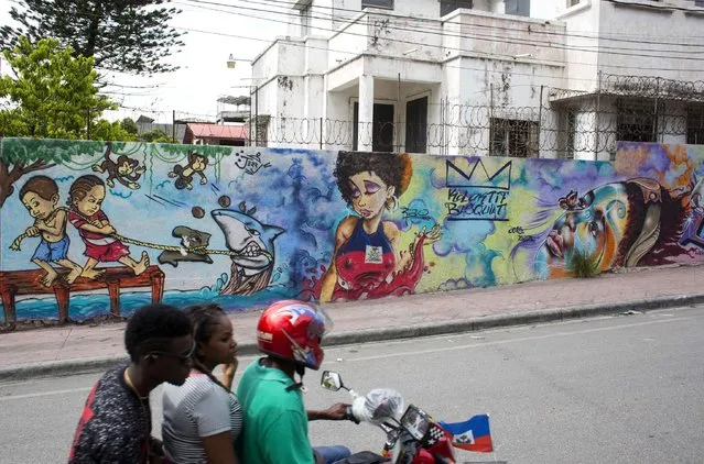 In this May 28, 2016 photo, a motorcycle taxi rides past a wall blanketed with murals in Petion-Ville, a suburb of Port-au-Prince, Haiti. (Photo by Dieu Nalio Chery/AP Photo)