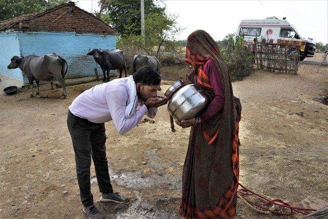 A village woman gives water to Sunil Kumar Naik, an ambulance driver, to quench his thirst during a heat wave, on the way to a hospital, near a village in Banpur in the Indian state of Uttar Pradesh, Saturday, June 17, 2023. Ambulance drivers and other healthcare workers in rural India are the first line of care for those affected by extreme heat. (Photo by Rajesh Kumar Singh/AP Photo)