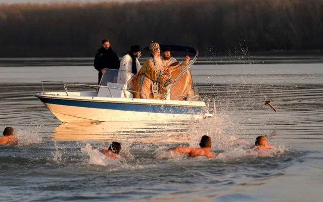 Orthodox archbishop Teodosie blesses throws a wooden cross in the Danube river as men swim to retrieve it during a religious service in Harsova, Romania, Sunday, January 5, 2020, a day ahead the celebration of Epiphany. More than 200 thousand bottles were filled with holy water in the Black Sea port of Constanta as Orthodox Romanians prepare to celebrate epiphany on Jan. 6. (Photo by Andreea Alexandru/AP Photo)
