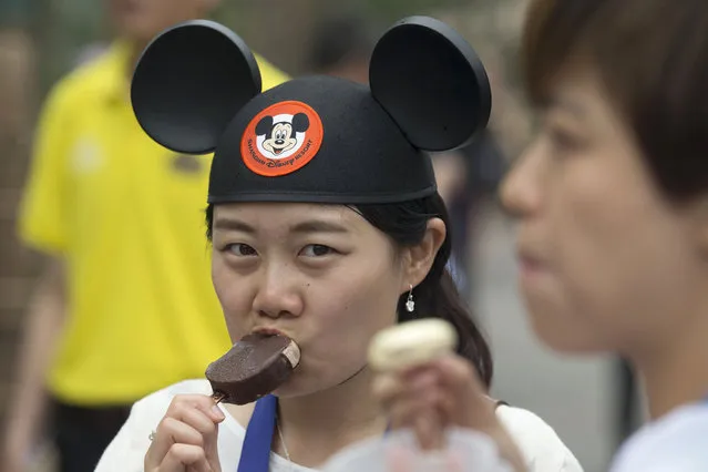 A visitor wearing a Mickey Mouse hat eats a Mickey Mouse-shaped ice cream during a tour on the eve of the opening of the Disney Resort in Shanghai, China, Wednesday, June 15, 2016. (Photo by Ng Han Guan/AP Photo)