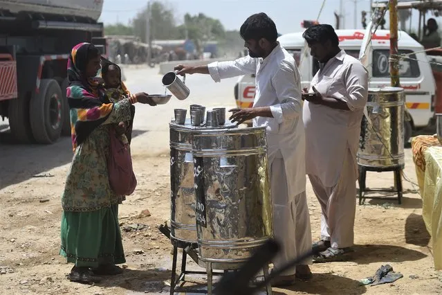 Volunteers distribute water to a woman carrying a child along a street during a hot summer day in Karachi on May 14, 2022.  (Photo by Rizwan Tabassum/AFP Photo)