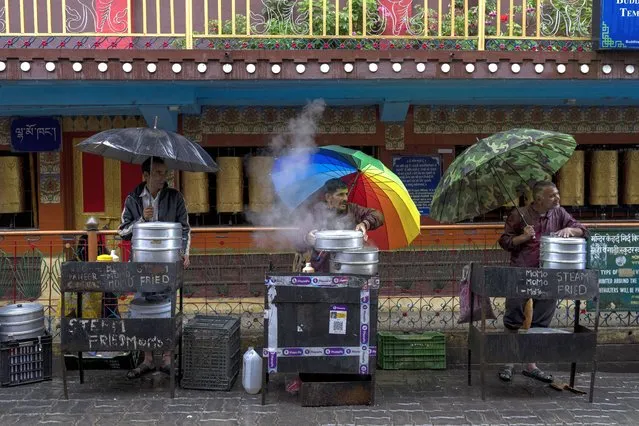 Vendors selling Tibetan dumplings woo customers as they protect themselves from rain in Dharmsala, India, Thursday, June 30, 2022. (Photo by Ashwini Bhatia/AP Photo)
