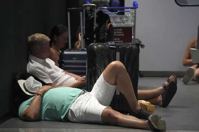 Passengers rest next to their luggage in Rome's Leonardo Da Vinci international airport, Sunday, July 17, 2022. Several hundred flights were canceled in Italy Sunday, a peak vacation travel day, because of four-hour walkouts involving employees of low-cost airlines as well as air traffic controllers. (Photo by Andrew Medichini/AP Photo)