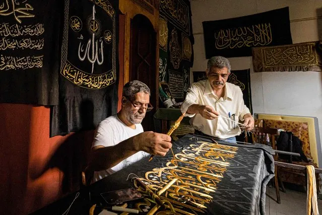 Egyptian embroiderer Ahmed Othman el-Kassabgy (R), whose family was traditionally responsible for used to be honoured with the task of producing the Kiswa, the cloth used to cover the Kaaba at the Grand Mosque in the Muslim holy city of Mecca, supervises as another employee (L) sews with gold thread a verse from the Holy Koran, Islam's holy book, onto a replica drape to be sold as a souvenir for tourists visiting the historic district of al-Hussein of Islamic Cairo in Egypt's capital on June 15, 2022. From the 13th century, Egyptian artisans made the giant cloth in sections, which authorities transported to Mecca with great ceremony. Celebrations would mark processions through cities, flanked by guards and clergymen as Egyptians sprinkled rosewater from balconies above. From 1927, manufacturing began to move to Mecca in the nascent Kingdom of Saudi Arabia, which would fully take over production of the kiswa in 1962. (Photo by Khaled Desouki/AFP Photo)