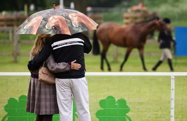A couple shelters from a rainfall underneath a horse-themed umbrella during The Royal Windsor Horse Show in Windsor, Britain on May 15, 2022. (Photo by Henry Nicholls/Reuters)