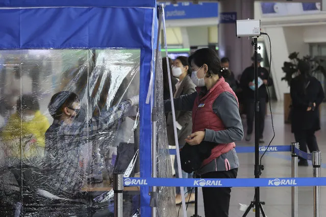 An employee of Korea Rail Road Corporation checks the temperature of a woman's wrist at the Seoul Railway Station in Seoul, South Korea, Saturday, March 21, 2020. (Photo by Ahn Young-joon/AP Photo)