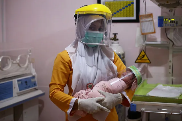 An Indonesian nurse wearing protective gear holds a newborn baby wearing a face shield as a protective measure amid the COVID-19 coronavirus pandemic at a clinic in Bireuen, Aceh province on April 15, 2020. (Photo by Amanda Jufrian/AFP Photo)