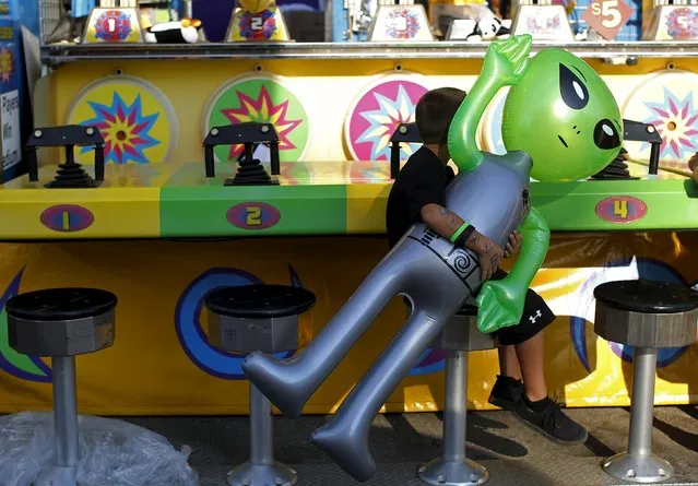 A boy carries an inflatable alien toy prize while sitting on a stool at the Iowa State Fair in Des Moines, Iowa, United States, August 15, 2015. (Photo by Jim Young/Reuters)