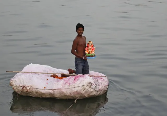 A boy holds an idol of the Hindu god Ganesh, the deity of prosperity, on a makeshift raft to immerse it in the waters of the river Sabarmati during the ten-day-long Ganesh Chaturthi festival in Ahmedabad, India, September 23, 2015. (Photo by Amit Dave/Reuters)