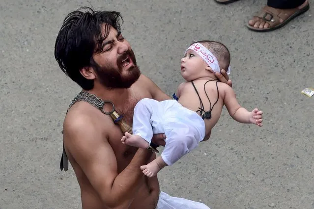 A Shiite Muslim holds his son before starting flagellating himself for an Ashura procession during the month of Muharram in Lahore on August 30, 2020. Ashura is a period of mourning for Shiite Muslims during Muharram commemorations to mark the seven-century martyrdom of Prophet Mohammad's grandson Imam Hussein who was killed in battle in Karbala in Iraq 680 AD. (Photo by Arif Ali/AFP Photo)