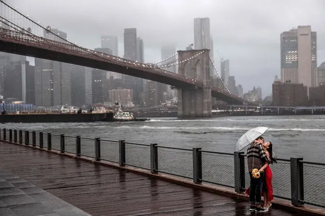 A couple poses for photos in front of the Brooklyn Bridge on a rainy Saturday, October 1, 2022, in New York. (Photo by Julia Nikhinson/AP Photo)