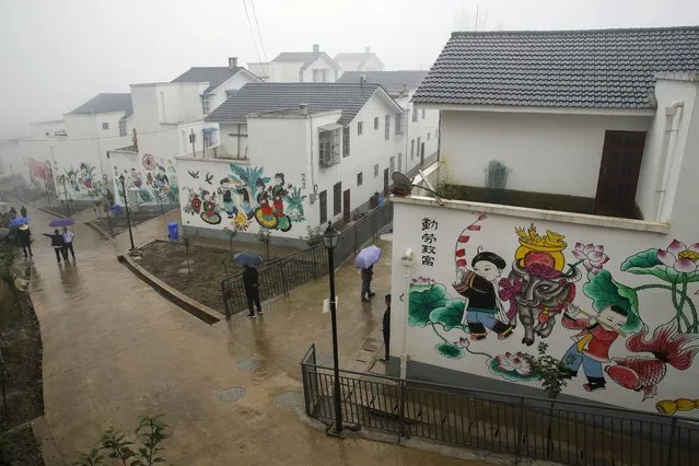 People walk by new village houses decorated with colourful paintings built by the Chinese government for ethnic minority members in Ganluo county, southwest China's Sichuan province on September 10, 2020. The ruling Communist Party says its initiatives have helped to lift millions of people out of poverty. Yi ethnic minority members were moved out of their mountain villages in China’s southwest and into the newly built town in an anti-poverty initiative. (Photo by Andy Wong/AP Photo)