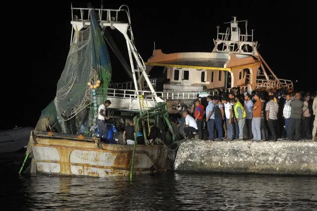 People gather on the quay as a wreck of a migrant boat raised by the Egyptian navy and maritime rescuers arrives in the Egyptian port city of Rosetta on September 27, 2016. The Egyptian military said 163 people had been rescued. The boat would have had at least 365 people on board when it went down en route to Italy, according to official figures. (Photo by AFP Photo/Stringer)