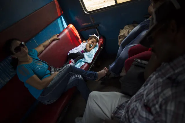 In this March 23, 2015 photo, a girl sleeps on a moving train with her family as they travel from Santiago de Cuba, to Santa Clara, in the Holguin province of Cuba. While the island is slowly modernizing its rail system, it remains the slowest way to get around already slow-moving Cuba. (Photo by Ramon Espinosa/AP Photo)