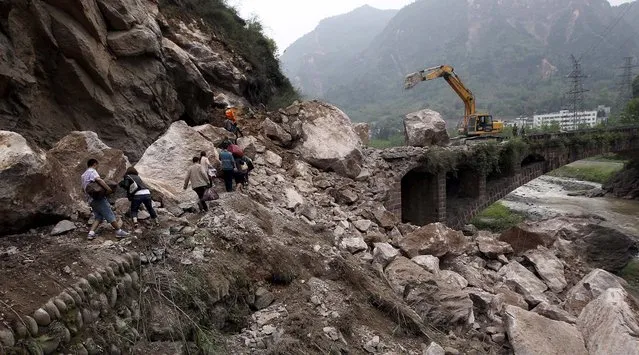 People walk over fallen rocks in Baosheng Township as repair crews work on a damaged bridge, on April 21, 2013. (Photo by Zhang Xiaoli/Xinhua)