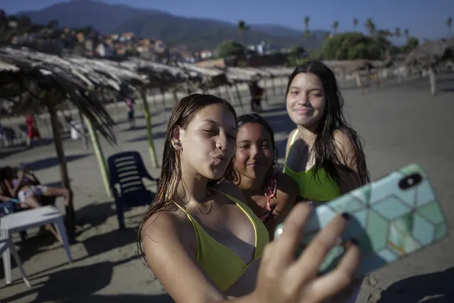 Friends take photos of themselves on La Ultima beach which was reopened this week after it was closed for months amid the COVID-19 pandemic in La Guaira, Venezuela, Friday, October 23, 2020. Strict quarantine restrictions forced the closure of beaches across the country in March and reopened this week in hopes of revitalizing the battered economy. (Photo by Matias Delacroix/AP Photo)