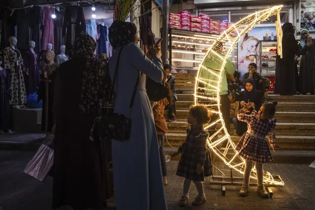 A Palestinian woman takes photos of her daughter next to a crescent moon-shaped decoration in a market, at the beginning of the Muslim holy month of Ramadan in Jebaliya refugee camp, northern Gaza Strip, Wednesday, March 22, 2023. (Photo by Fatima Shbair/AP Photo)