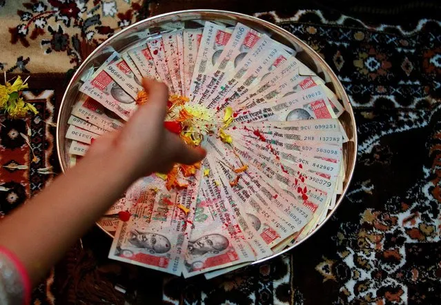 A woman puts flower petals on 1000 Indian rupee notes as she prays as part of a ritual during Dhanteras, a Hindu festival associated with Lakshmi, the goddess of wealth, in Ahmedabad, India October 28, 2016. (Photo by Amit Dave/Reuters)