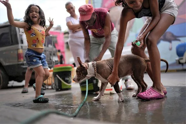 A girl bathes her dog, next to her sister on a street of the San Agustin neighborhood of Caracas, Venezuela, Monday, April 3, 2023. (Photo by Matias Delacroix/AP Photo)