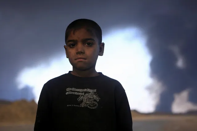 A boy poses for the camera as smoke rises from oil wells, set ablaze by Islamic State militants before the militants fled the oil-producing region of Qayyara, Iraq, November 12, 2016. (Photo by Air Jalal/Reuters)