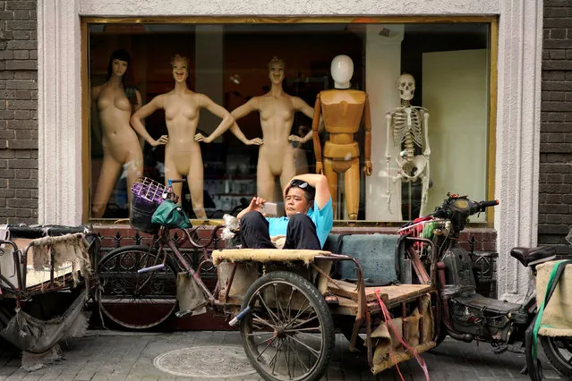 A man looks at his mobile phone on a tricycle outside a mannequin shop in Shanghai, China on June 25, 2018. (Photo by Aly Song/Reuters)