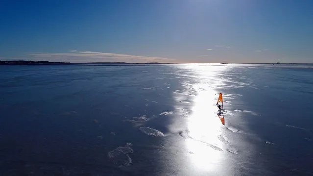 An aerial photo taken on February 28, 2021 shows an ice surfer skating across the frozen Baltic Sea off the coast of Helsinki. What to do if you are a windsurfing enthusiast in a country where the sea freezes over for months of the year? For a group of Finns, the answer is to kit out sailboards with skates and take to the ice, reaching speeds of up to 100km/h (62mph) in a burgeoning sport that can only be practised in a handful of places around the world. (Photo by Sam Kingsley/AFP Photo)