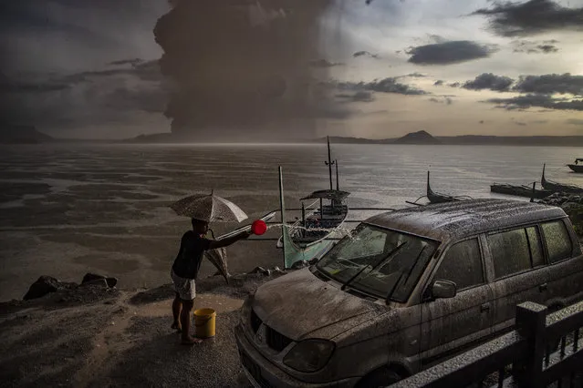 In this image released by World Press Photo, Thursday April 15, 2021, by Ezra Acayan for Getty Images, part of a series titled Taal Volcano Eruption, which won second prize in the Nature Stories category, shows A resident of Talisay in Batangas washes down a car, which is covered in volcanic ash mixed with rain, as Taal Volcano erupts, Batangas, Philippines, on Jan. 12, 2020. (Photo by Ezra Acayan for Getty Images, World Press Photo via AP Photo)