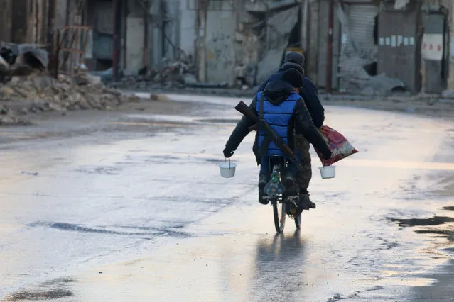 A rebel fighter carries food while riding a bicycle and carrying his weapon on his back in rebel-held besieged old Aleppo, Syria December 2, 2016. (Photo by Abdalrhman Ismail/Reuters)