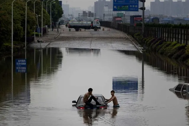 This picture taken on April 7, 2015 shows two men attempting to push a car out of floodwaters after a storm swept Changsha, central China's Hunan province. (Photo by AFP Photo/Stringer)