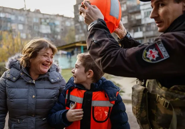 A member of the White Angel unit of Ukrainian police takes a helmet off Denys, 11, an internally displaced person (IDP) from the town of Toretsk, who arrived at a temporary shelter after evacuation with his mother Olha, amid Russia's attack on Ukraine, in Kostiantynivka, Donetsk region, Ukraine on November 13, 2023. (Photo by Alina Smutko/Reuters)