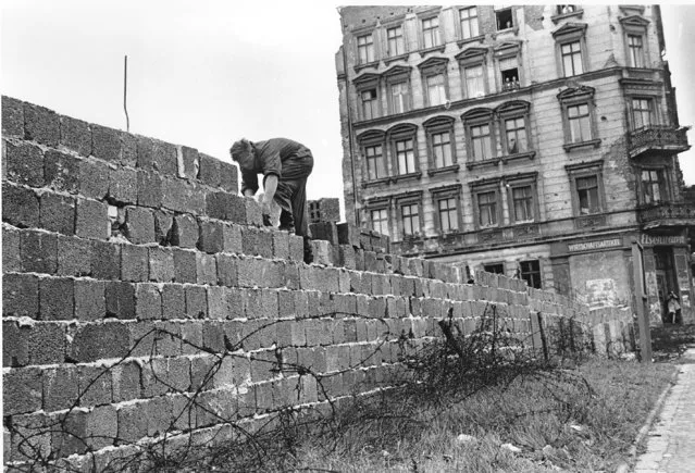 An East Berlin policeman puts bricks in place as the Berlin Wall is heightened to 15 feet, 5 m, separating East and West Berlin, Germany, on September 9, 1961. People watch from their apartment building windows in background above. (Photo by AP Photo)