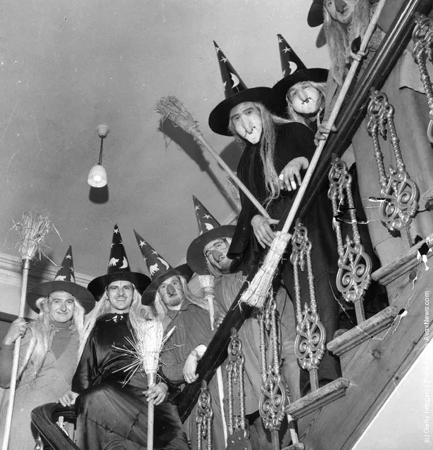 1950: A group of men in costume as witches, complete with brooms, to celebrate Halloween, line the staircase of a house