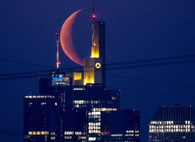 The moon rises behind the buildings of the banking district in Frankfurt, Germany, Monday, March 28, 2022. (Photo by Michael Probst/AP Photo)