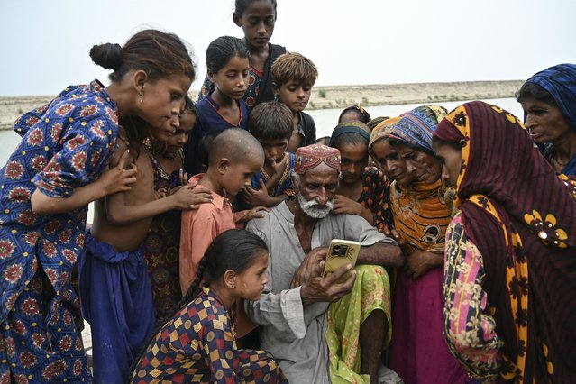 In this photograph taken on August 3, 2024 villagers gather to view a video on a social media platform at Khan Muhammad Mallah village, Dadu district in Sindh province. As monsoon rains were about to break over Pakistan, 14-year-old Shamila and her 13-year-old sister Amina were married off in exchange for money, a decision their parents made to help the family survive the threat of floods. Pakistan's high rate of marriages for underage girls had been inching lower in recent years, but after unprecedented floods in 2022 rights workers warn such weddings are now on the rise due to climate-driven economic insecurity. (Photo by Asif Hassan/AFP Photo)