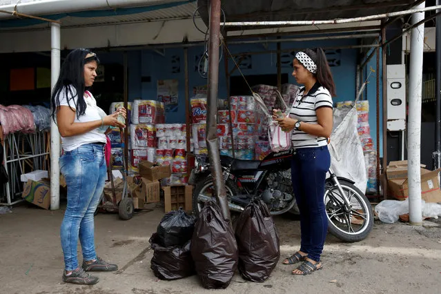 Women holding Venezuelan bolivar notes talk in front of a store that sells food and staple items in Puerto Santander, Colombia, June 3, 2016. (Photo by Carlos Garcia Rawlins/Reuters)