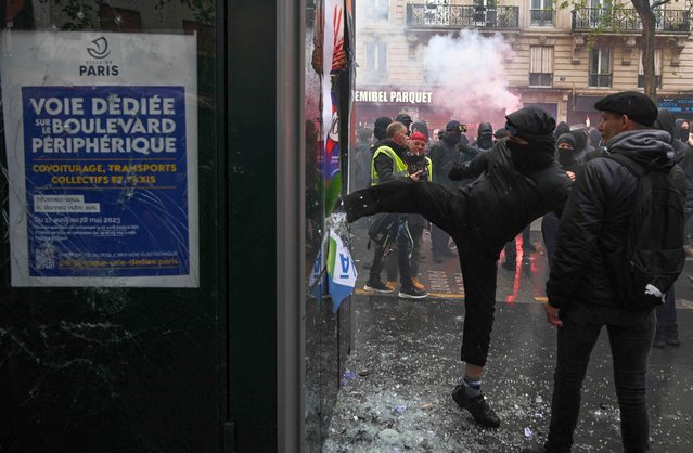 A protestor kicks a kiosk during a demonstration on May Day (Labour Day), to mark the international day of the workers, more than a month after the government pushed an unpopular pensions reform act through parliament, in Paris, on May 1, 2023. Opposition parties and trade unions have urged protesters to maintain their three-month campaign against the law that will hike the retirement age to 64 from 62. (Photo by Alain Jocard/AFP Photo)