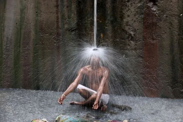 A man cools off under a pipe of flowing water on a hot summer day in New Delhi, India, May 11, 2022. (Photo by Anushree Fadnavis/Reuters)