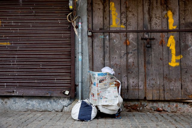 A man reads a newspaper on a sidewalk in the old quarters of Delhi, India on August 27, 2024. (Photo by Ainnie Arif/Reuters)