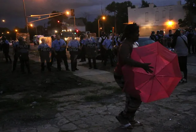 A lady crosses in front of the police line as they stand guard in riot gear where protesters gather on Walton Avenue and Page Boulevard on Wednesday, August 19, 2015, in St. Louis. (Photo by Laurie Skrivan/St. Louis Post-Dispatch via AP Photo)