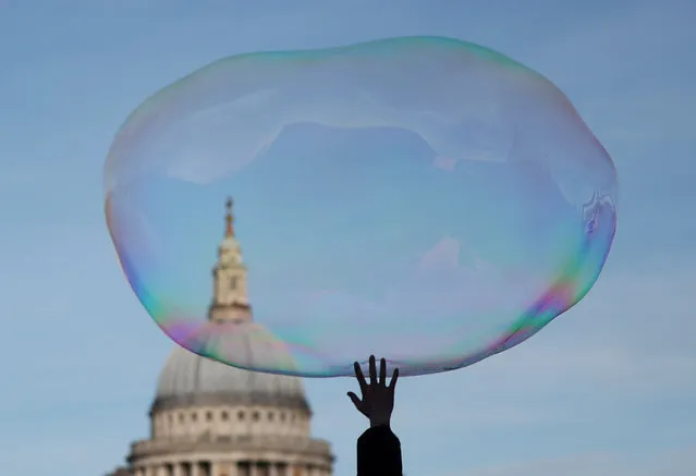 A child bursts a soap bubble as it floats past St Paul's Cathedral in London, Britain, December 27, 2019. (Photo by Hannah McKay/Reuters)