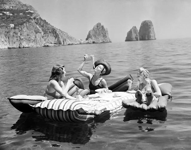 Unsettled life in Europe failed to change the slow pace of life on the Isle of Capri, off Naples, Italy. Some of the socialites who have come there to relax enjoy an aquatic luncheon serviced in the cool Mediterranean, September 1, 1939. Swimming waiters push out the floating tables bearing meals which include wine and spaghetti. In the background are the rocks of Faraglioni. (Photo by Hamilton Wright/AP Photo)