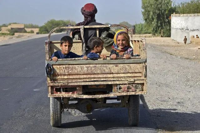 In this photograph taken on August 29, 2022, children travel at the back of a vehicle along a street in Kandahar. (Photo by Javed Tanveer/AFP Photo)