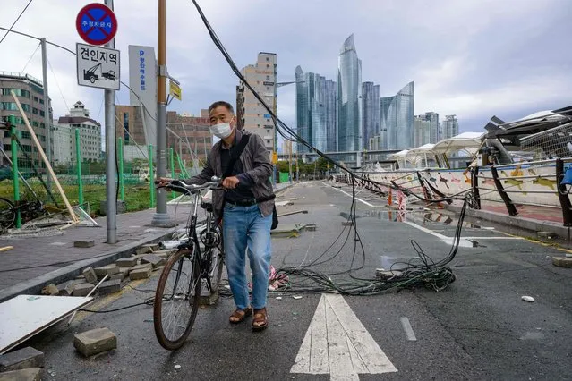 A man pushes his bicycle under a damaged electric cable on a road after Typhoon Hinnamnor passed through Busan on September 6, 2022. (Photo by Anthony Wallace/AFP Photo)