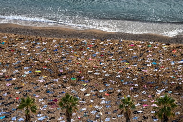Journalists take pictures of the boat and the clothes planted on the sand of the beach at dawn on December 11, 2023 in Barcelona, Spain. The charity assembled clothes representing the more than 2,600 women, men and children who have drowned attempting to cross the Mediterranean this year to reach European coasts. (Photo by Zowy Voeten/Getty Images)