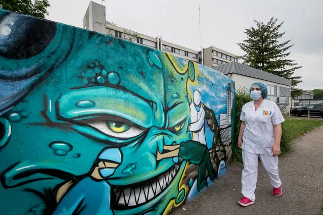 Medical staff members walk past a mural depicting a nurse, a doctor and a soldier fighting against the COVID-19 pandemic, painted by street artist Slimjoe in support of health workers, outside the Emilie Muller Hospital in Mulhouse, eastern France, on May 22, 2020. (Photo by Sebastien Bozon/AFP Photo)