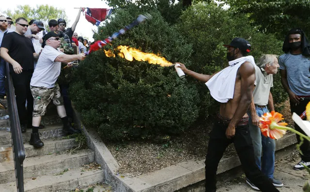 A counterprotester uses a lighted spray can against a white nationalist protester at the entrance to Lee Park in Charlottesville, Va., on August 12, 2017. The white nationalists were holding the rally to protest plans by the city of Charlottesville to remove a statue of Confederate Gen. Robert E. Lee. Gov. Terry McAuliffe declared a state of emergency after chaotic violent clashes broke out between the groups. (Photo by Steve Helber/AP Photo)